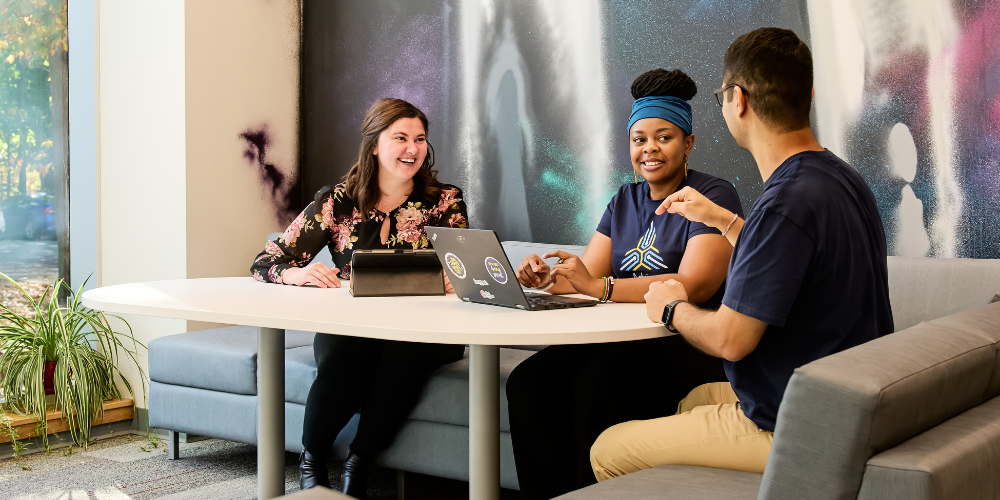 Three people sit together conversing and working