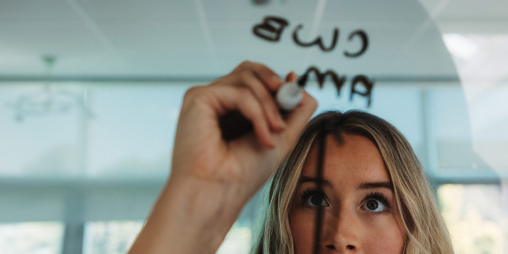 A person is writing notes on a transparent blackboard