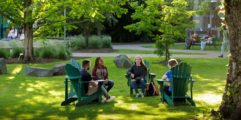 Students sit on chairs outdoors in a sunny, green quad on campus