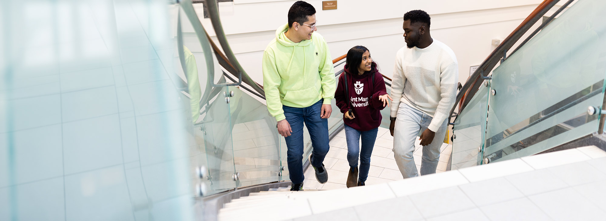 Three smiling students walking up the stairs.