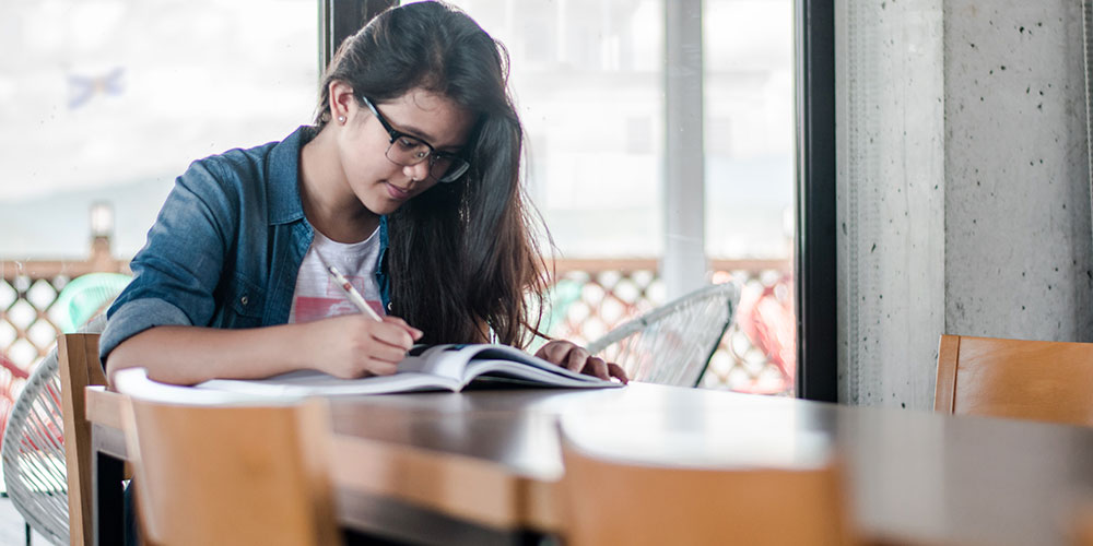 A young person in a SMU t-shirt sits at a table doing work.