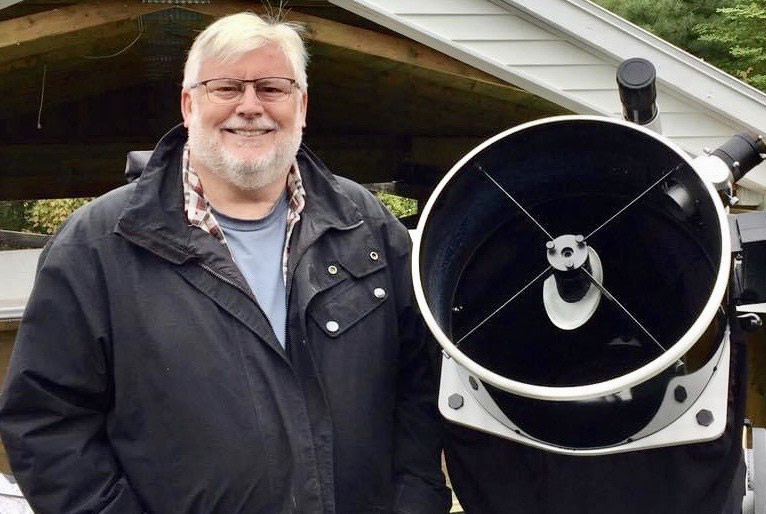 David Chapman stands beside a telescope.